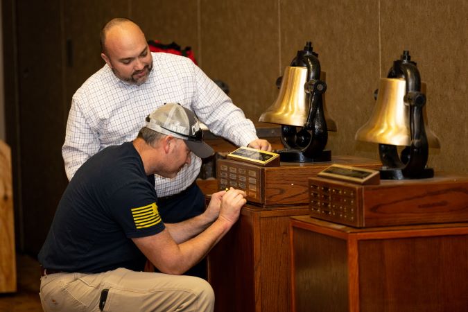 Heartland Division General Manager Tony Fulton watches as Aaron Stich, electrician, applies a nameplate to one of their bells. 